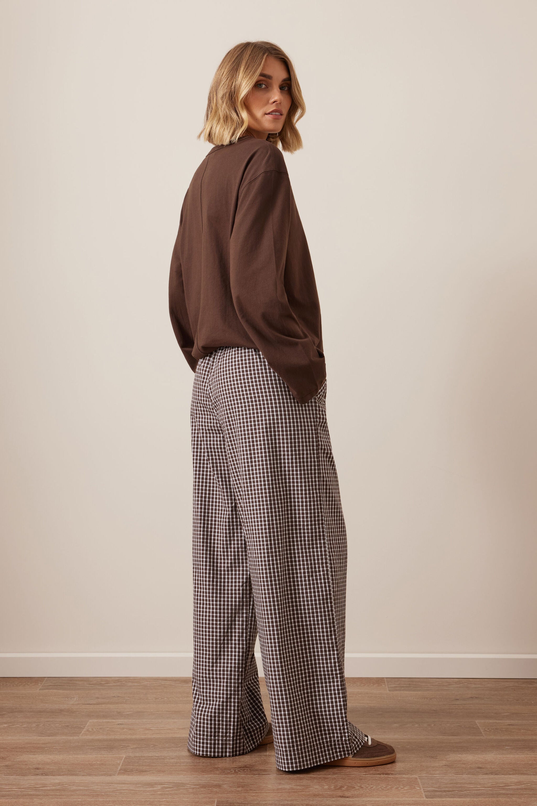 Back three-quarter view of woman in chocolate check lounge pants with brown sweater