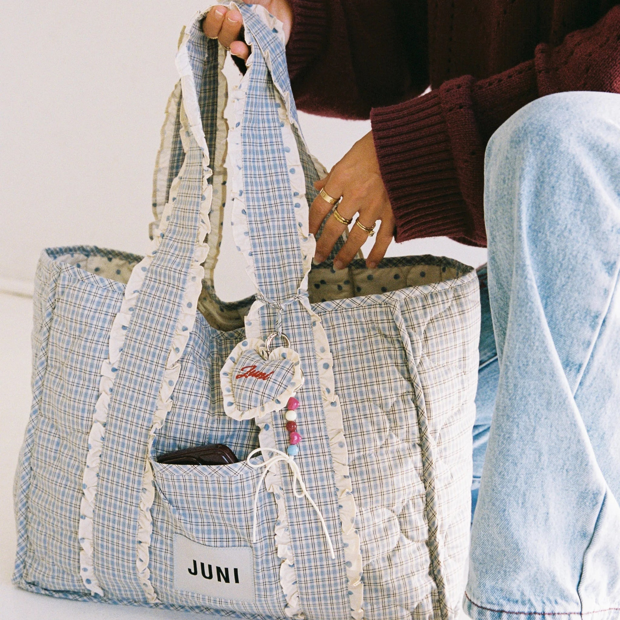 Person holding a blue and white checkered bag with 'JUNI' branding.