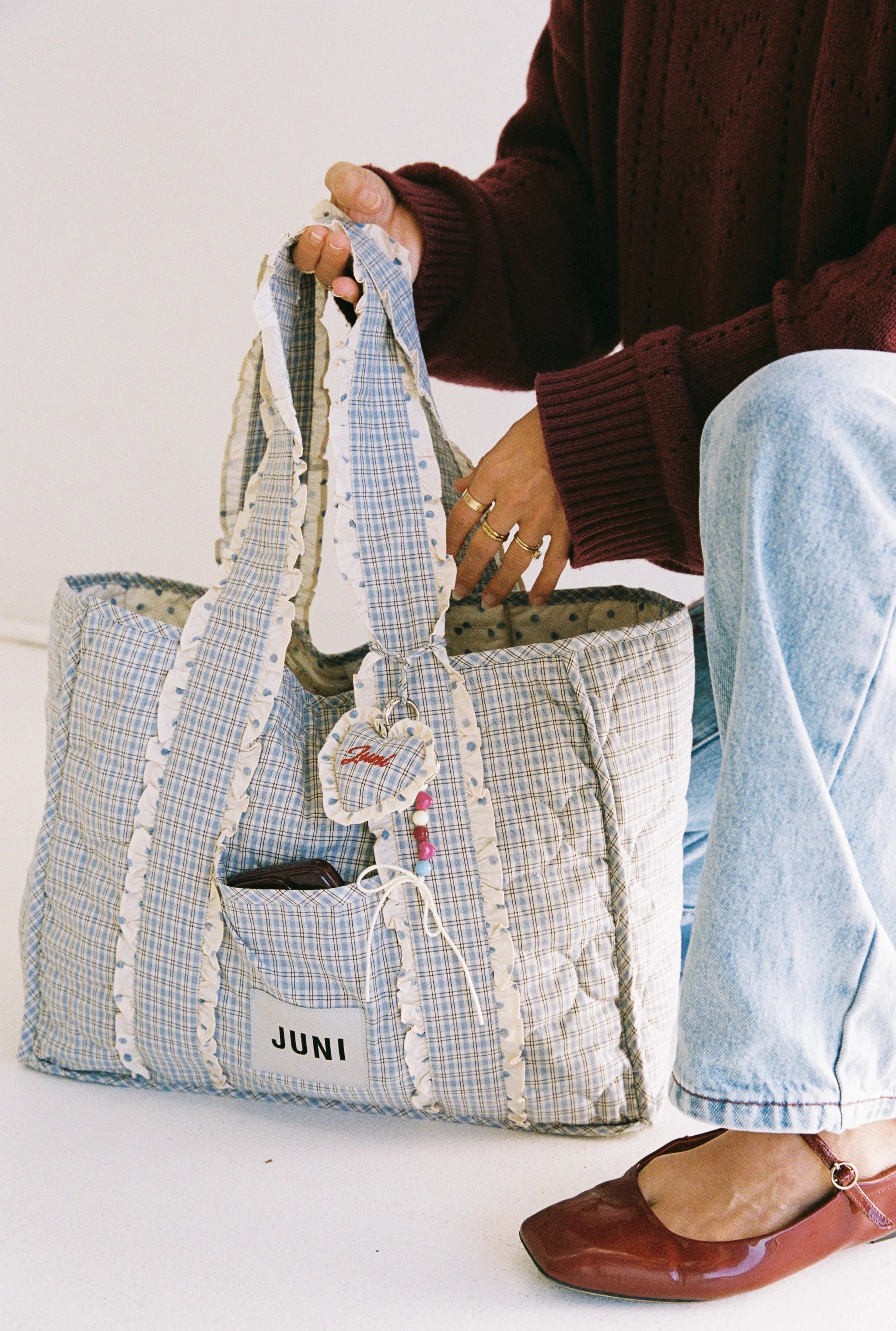 Person holding a blue and white checkered bag with 'JUNI' branding.