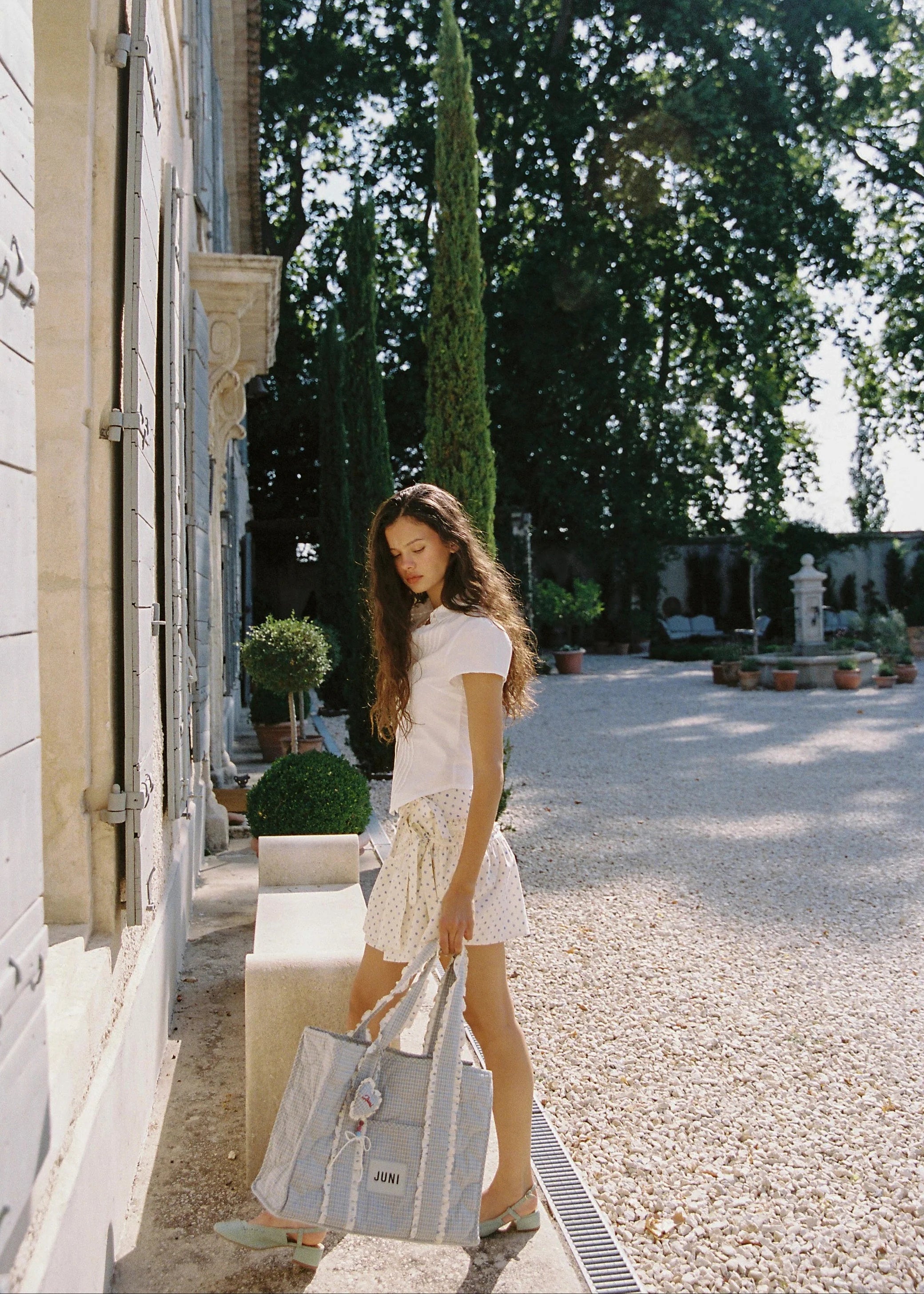 Woman holding a large bag in an outdoor setting with trees and a building.