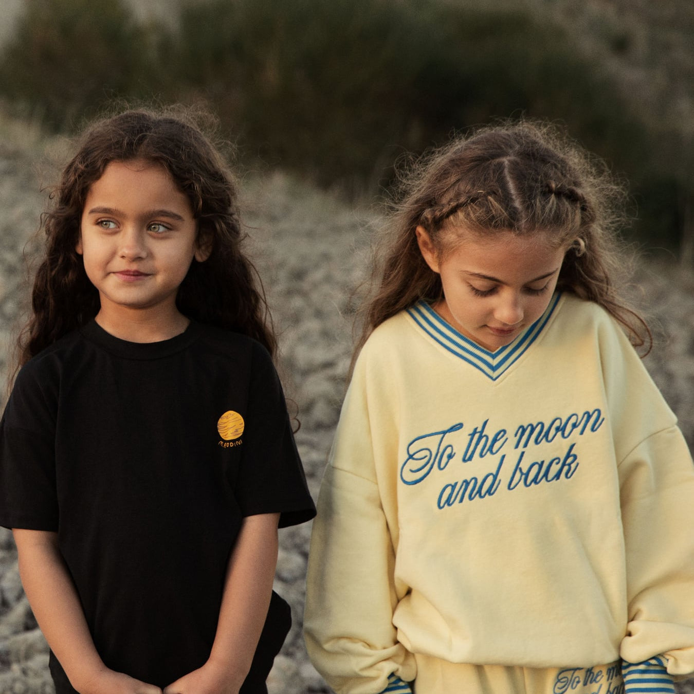 Two children wearing mini rodini To the Moon collection in outdoor natural setting