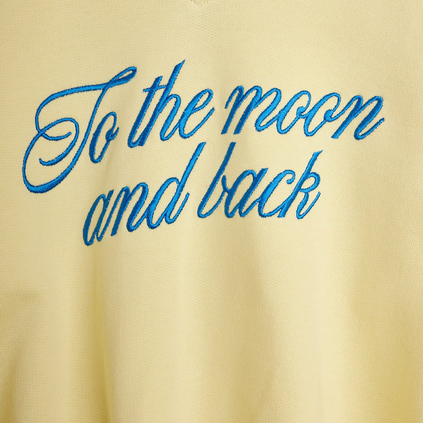 Close-up detail of blue embroidered To the Moon and back script lettering on yellow fabric