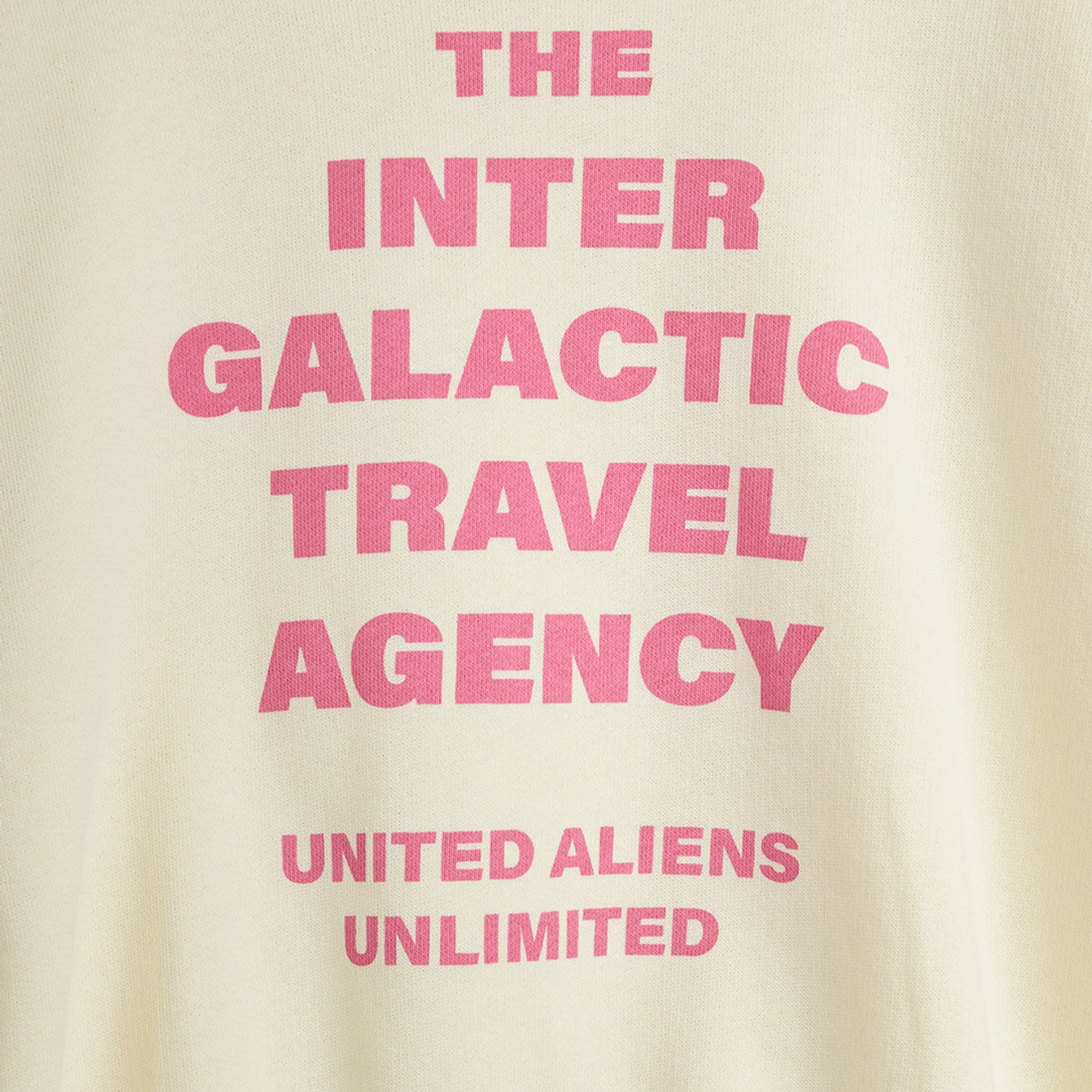 Close-up of pink Inter Galactic Travel Agency text print on off-white sweatshirt fabric