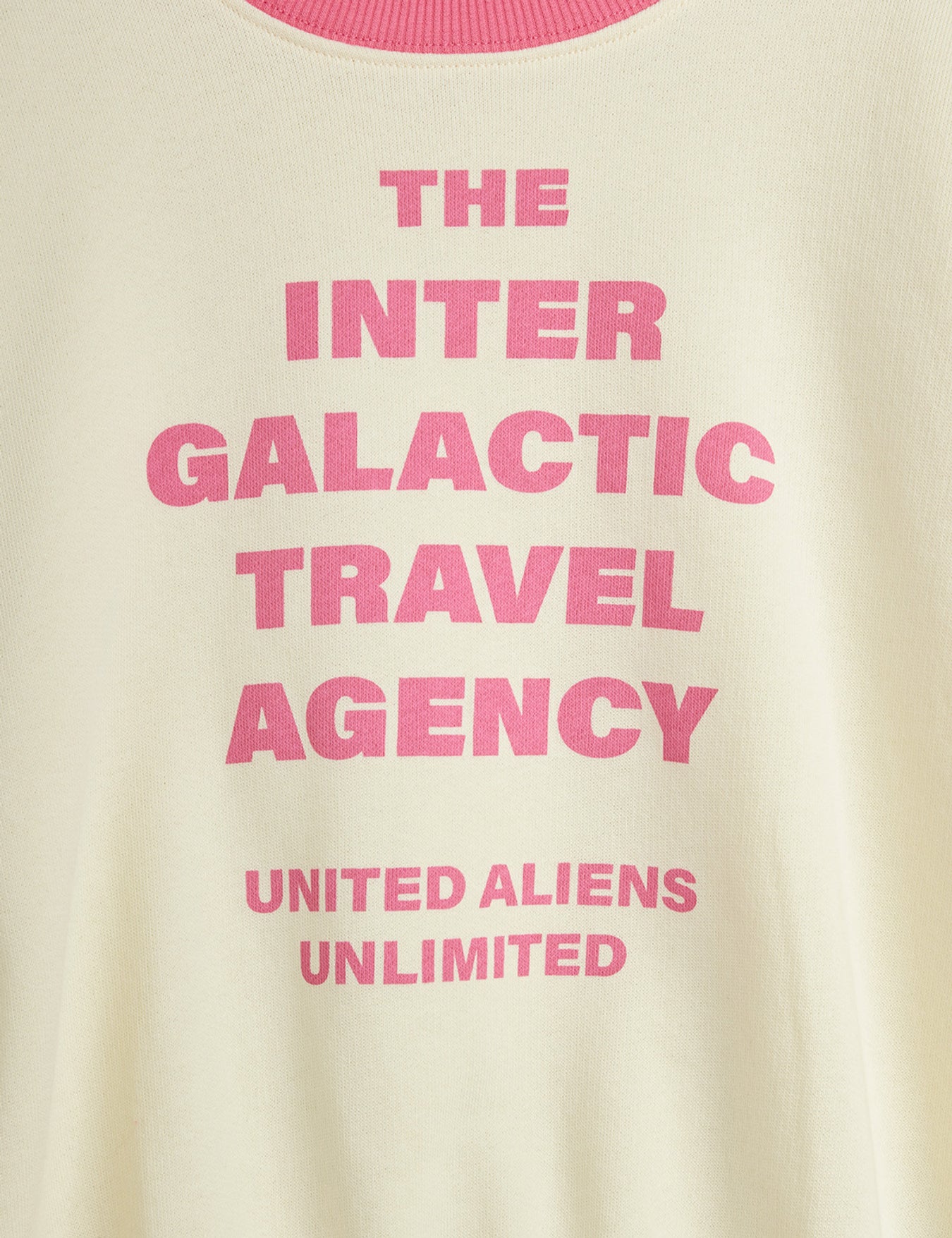 Close-up of pink Inter Galactic Travel Agency text print on off-white sweatshirt fabric