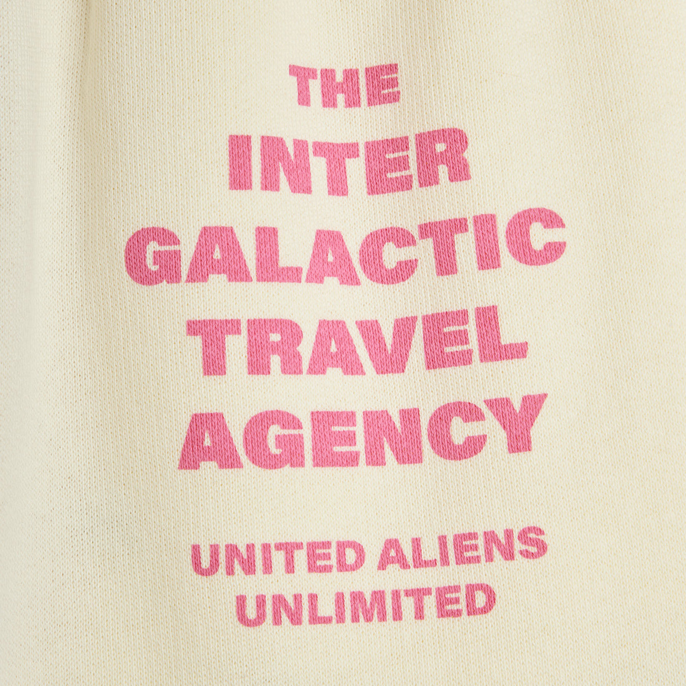 Close-up of Inter Galactic Travel Agency text print in pink lettering on cream fabric