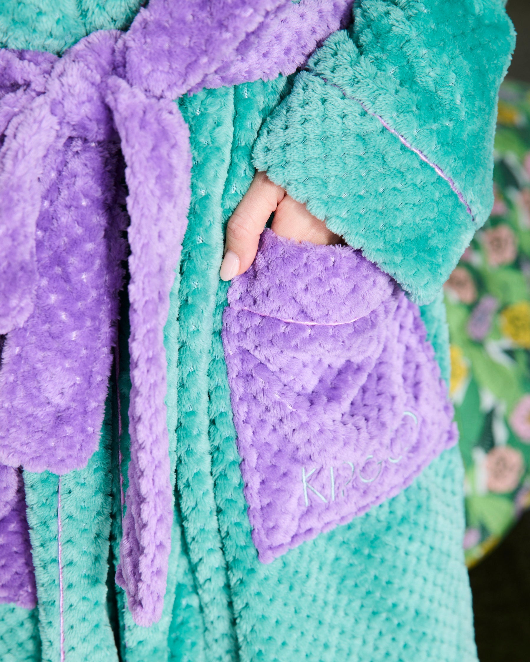 Close-up detail of Tropicas Cosy Robe showing teal textured fabric, purple pocket and branded belt