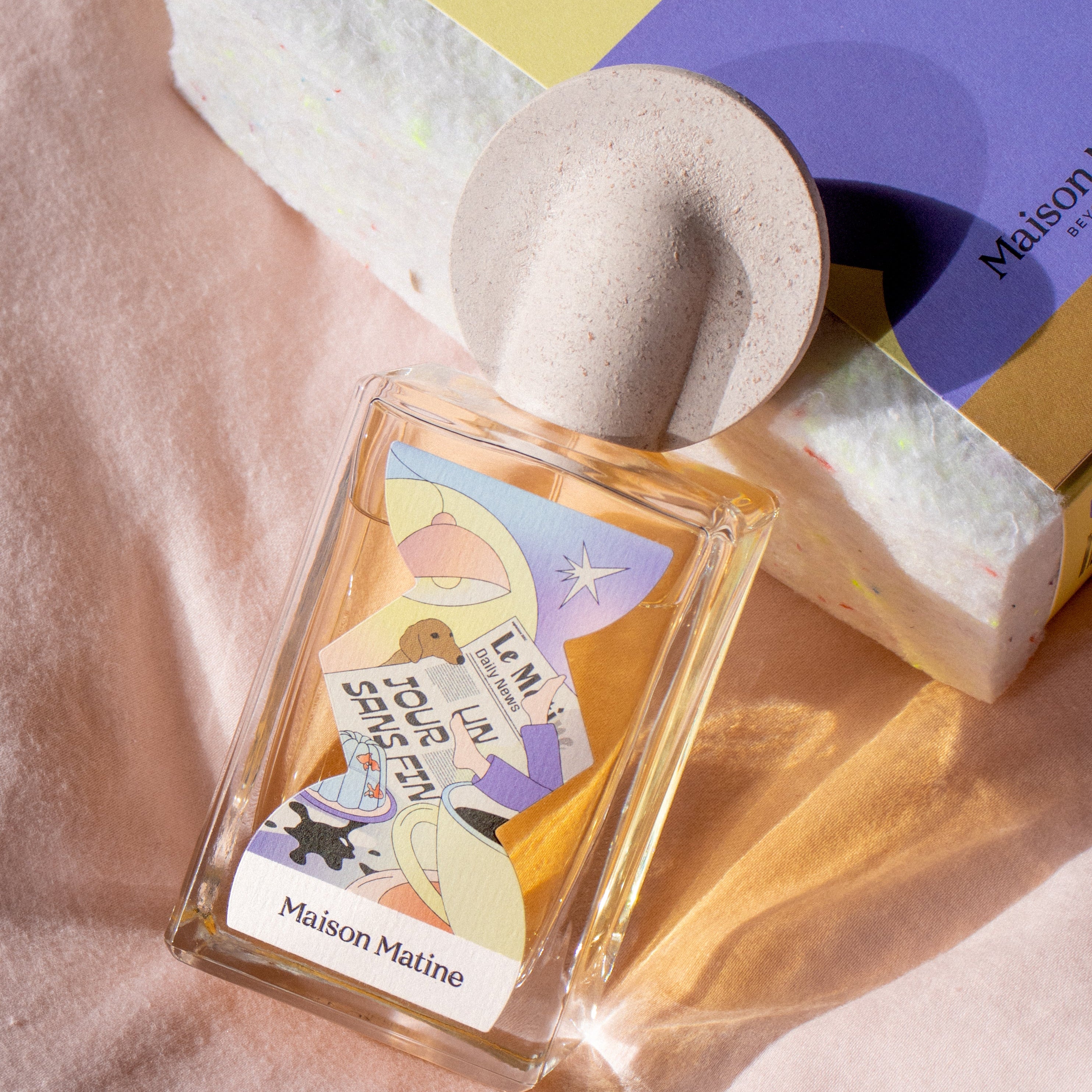 Un Jour Sans Fin perfume with speckled pink cap displayed with packaging box in natural lighting