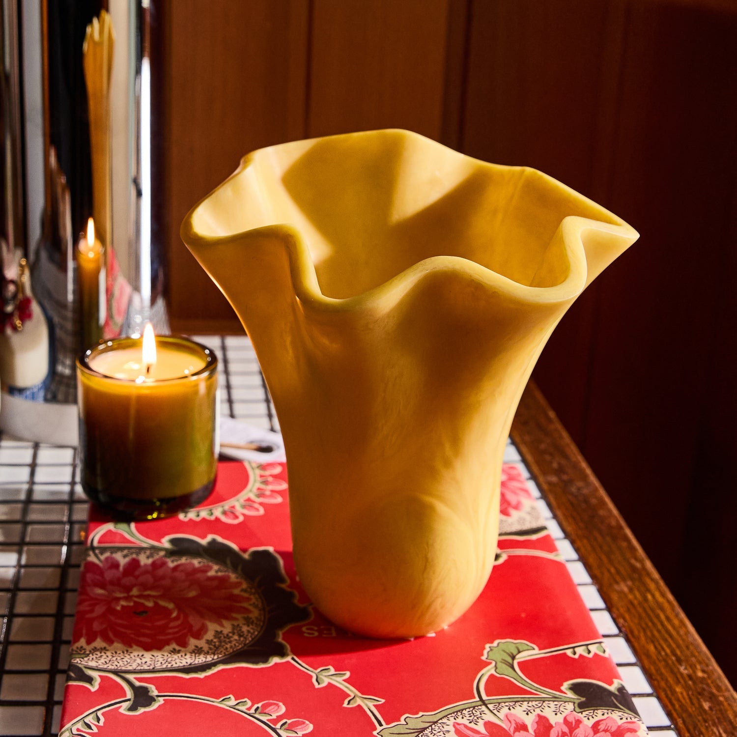 Close-up of the Aspen Gold Violetta Vase with ruffled wavy rim, styled on a floral runner with a candle