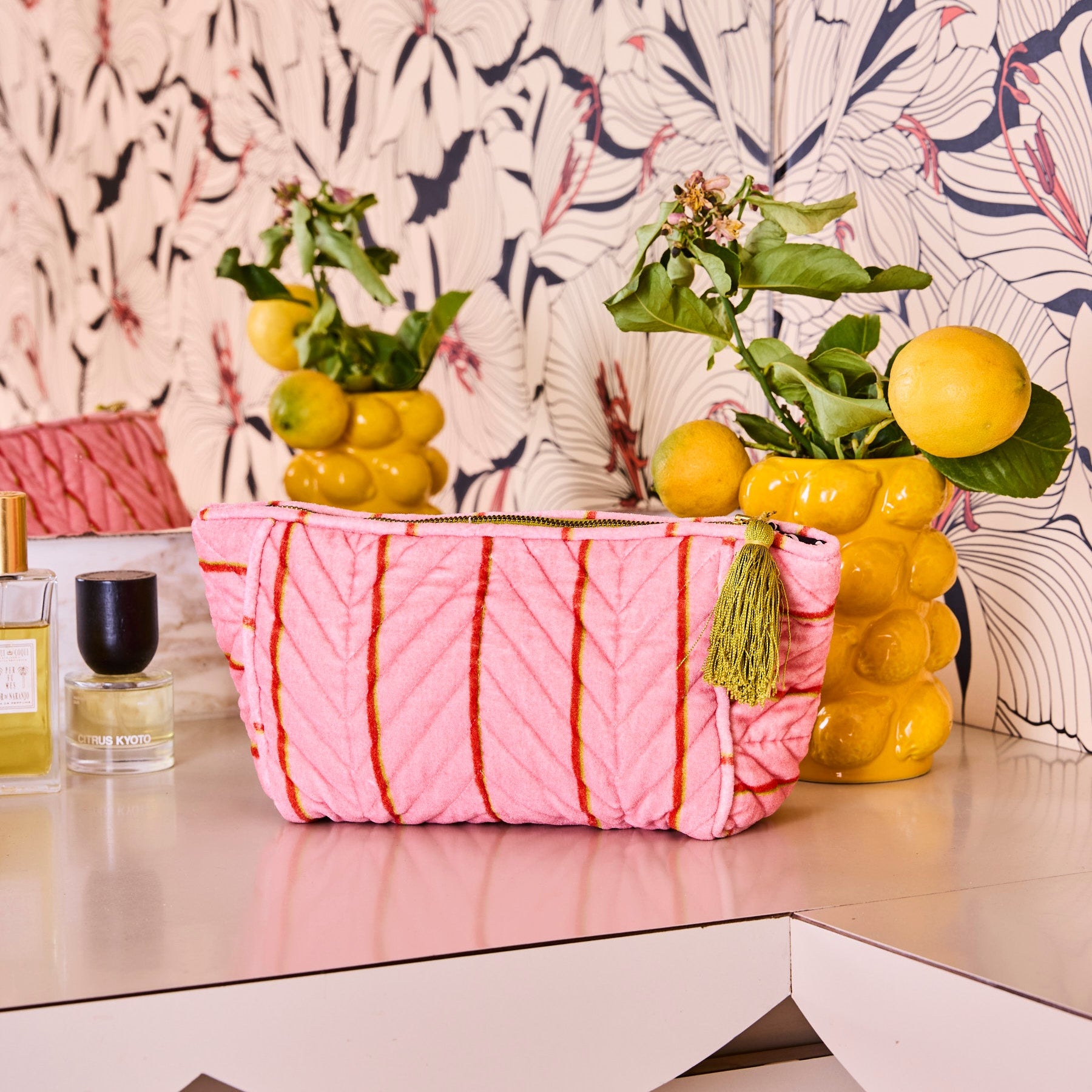 Kip & Co Wategos Soiree Stripe pink velvet toiletry bag styled on vanity with tropical wallpaper and gold tassel
