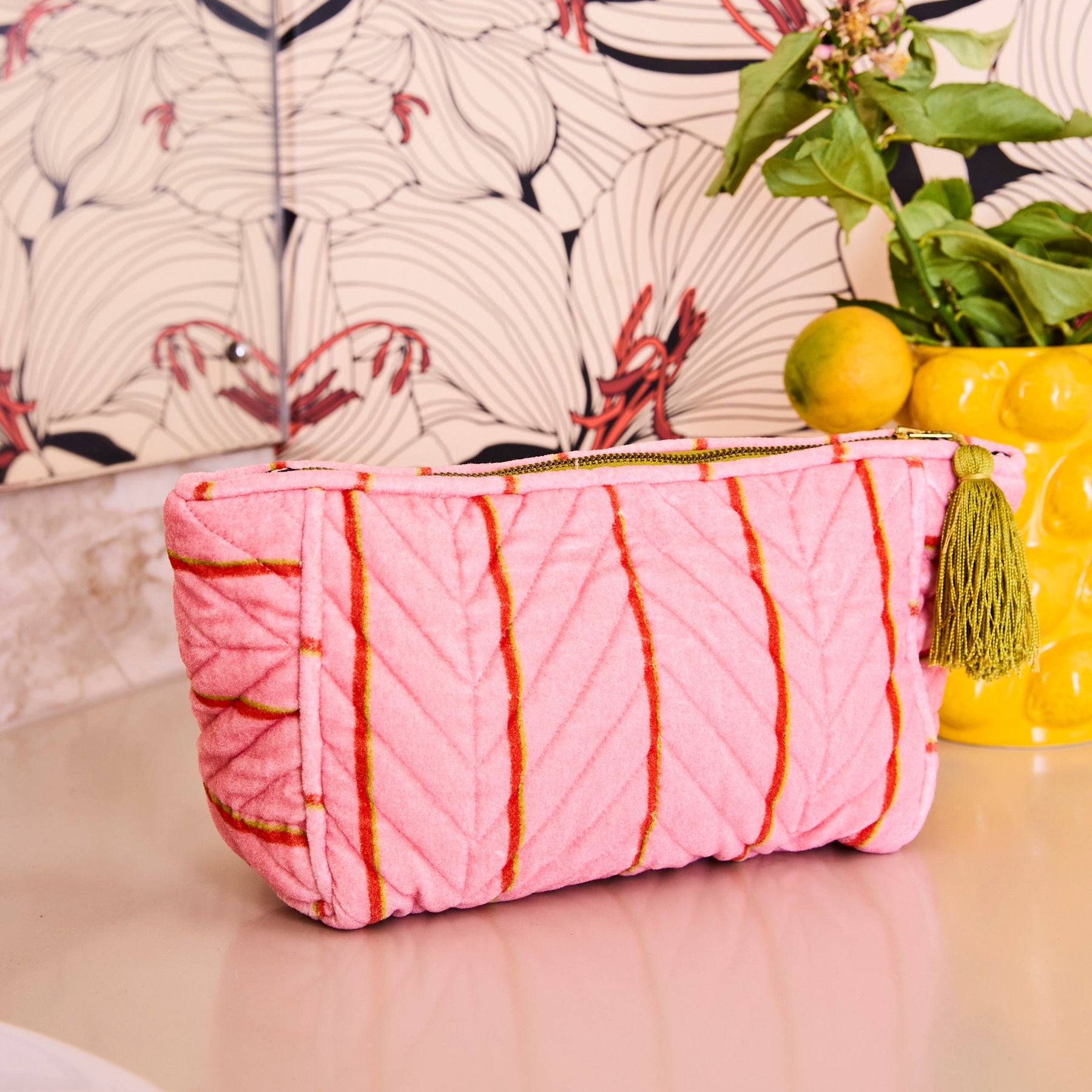 Side angle view of pink velvet striped Wategos Soiree toiletry bag showing quilted texture and gold tassel detail