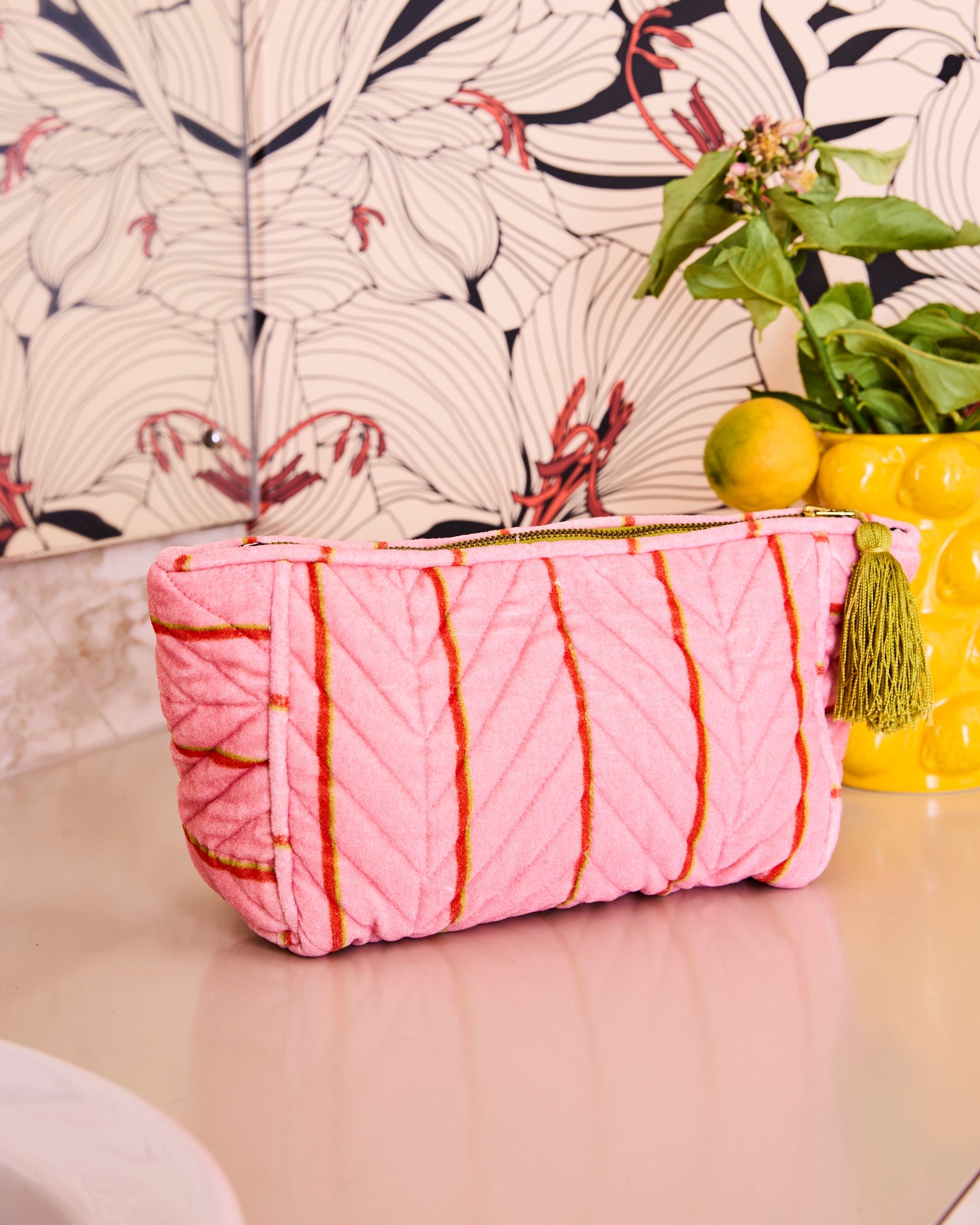 Side angle view of pink velvet striped Wategos Soiree toiletry bag showing quilted texture and gold tassel detail