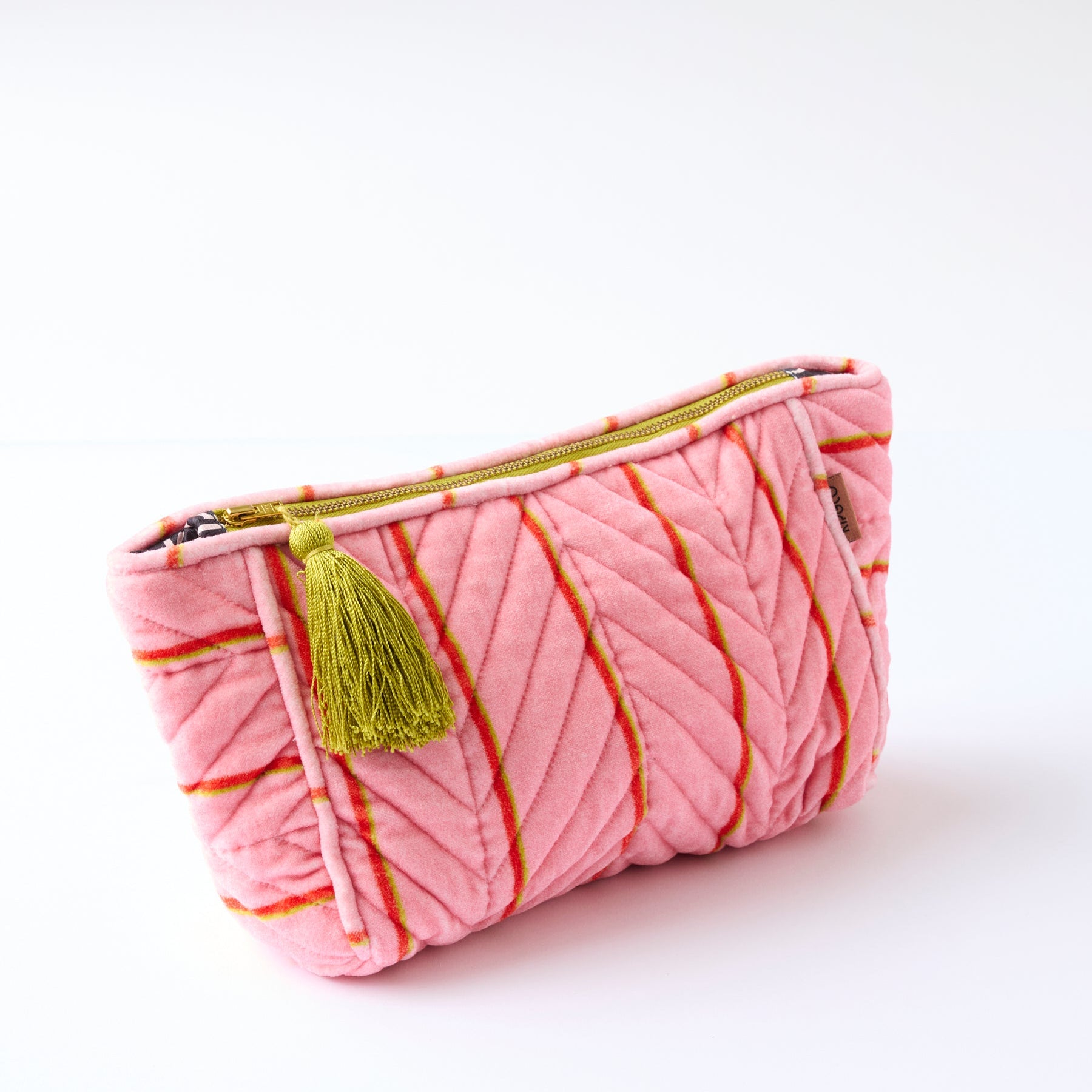 Close-up of Kip & Co pink velvet toiletry bag showing quilted stripe pattern and zipper with tassel charm