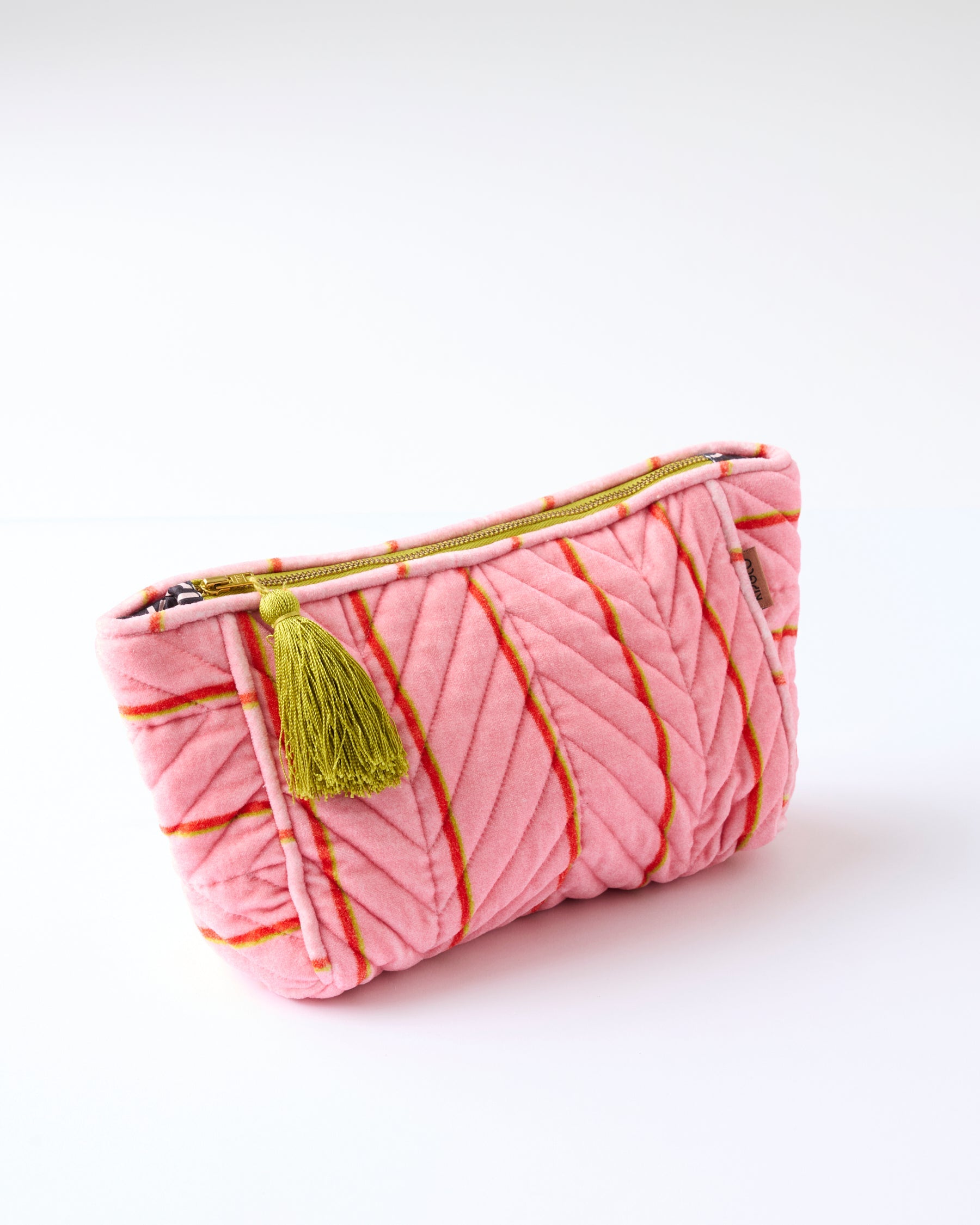 Close-up of Kip & Co pink velvet toiletry bag showing quilted stripe pattern and zipper with tassel charm