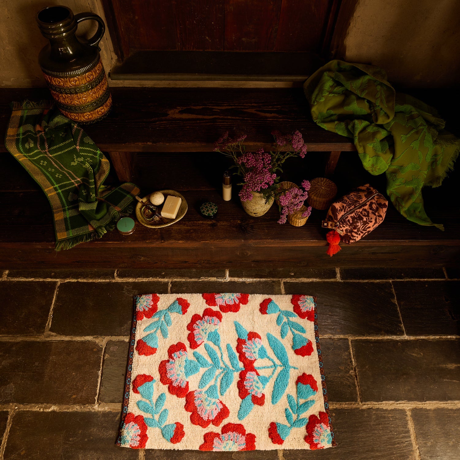 Moonlight Winona Bath Mat on dark stone floor, overhead angle showing cream base with bold red and teal floral tufted pattern