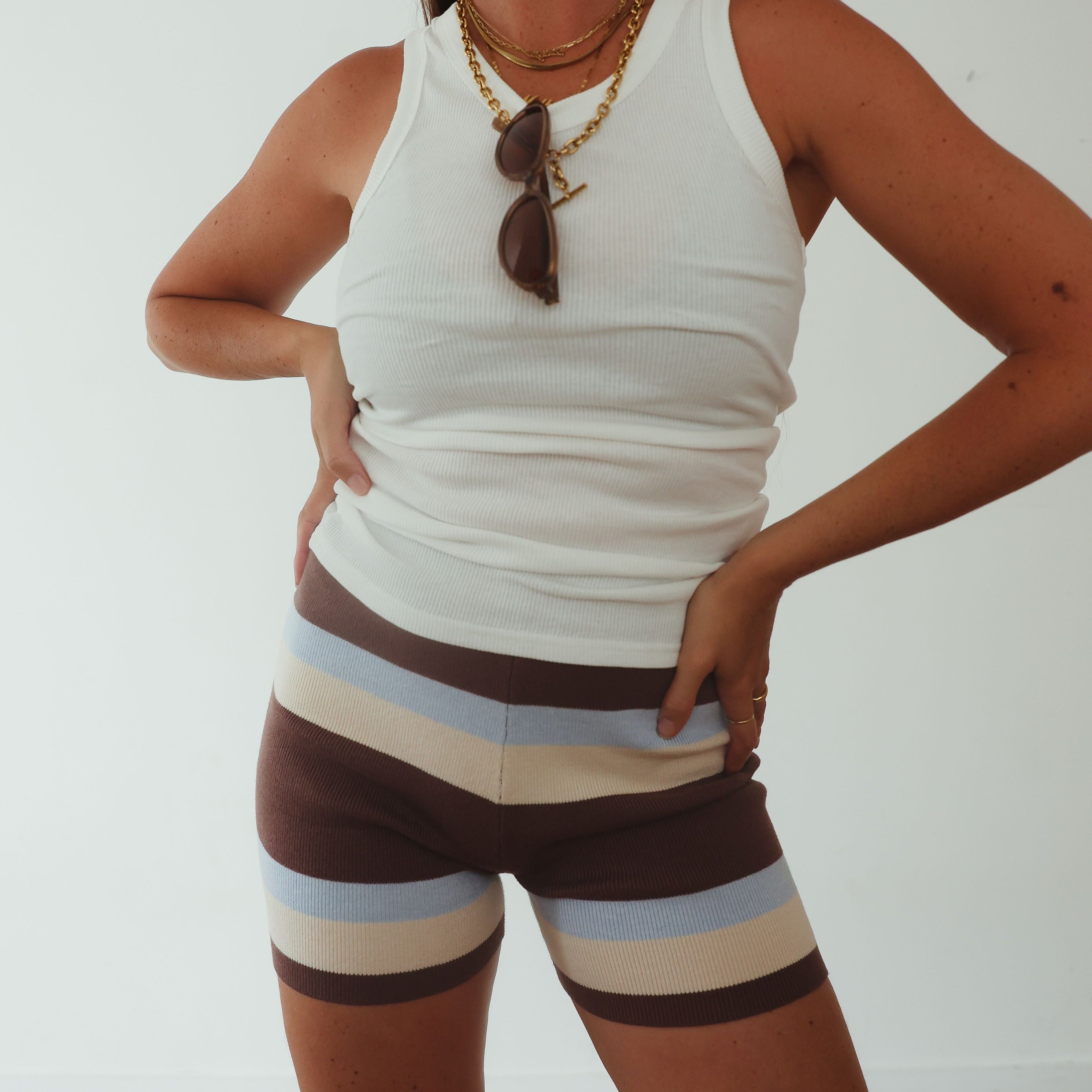 Beach lifestyle shot of brown, cream and blue striped knit shorts styled with white cami top