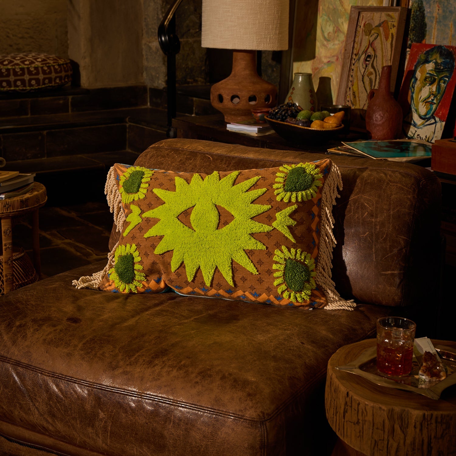 Brown patterned lumbar cushion with lime green tufted star motifs and corner sunflower details on a leather sofa