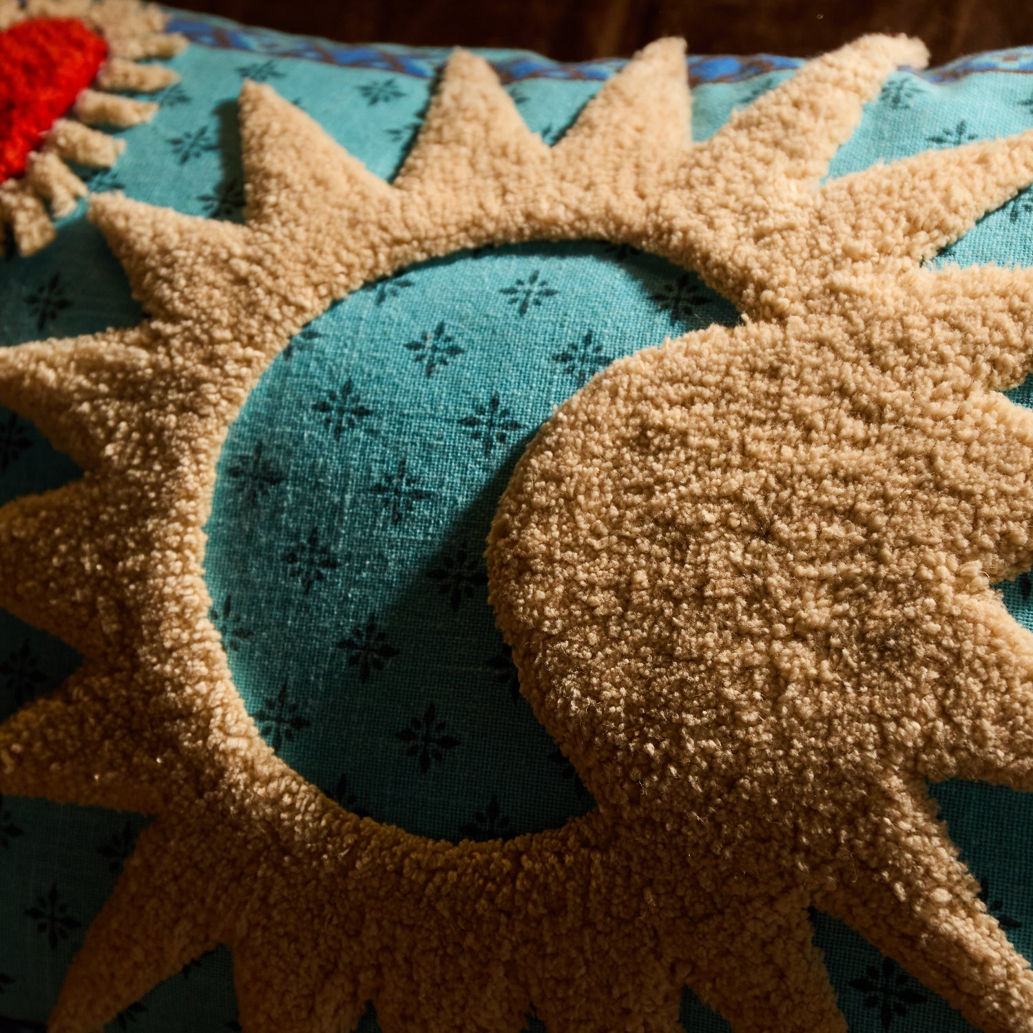 Close-up of cream tufted sun and crescent moon detail on a turquoise patterned cushion cover