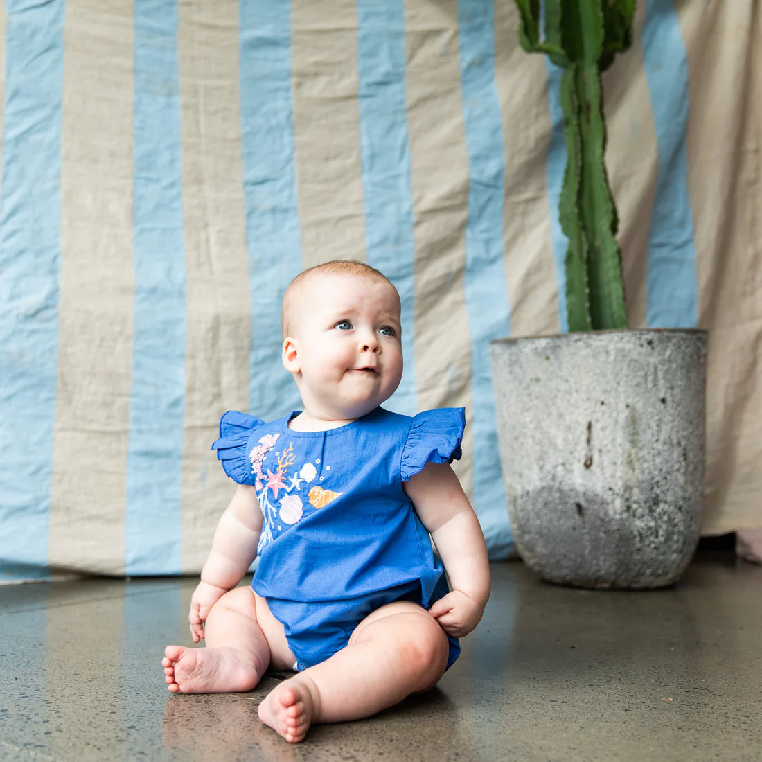 baby wearing Yasmin Romper-Yves Klien by Pearson & Pearson - blue coloured cotton with pastel coloured coral embroidery