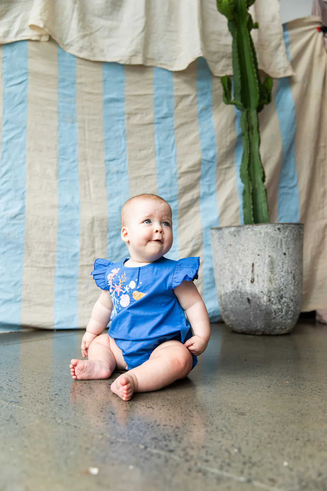 baby wearing Yasmin Romper-Yves Klien by Pearson & Pearson - blue coloured cotton with pastel coloured coral embroidery