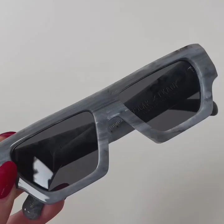 Gray glasses held by a hand with red nail polish against a plain background