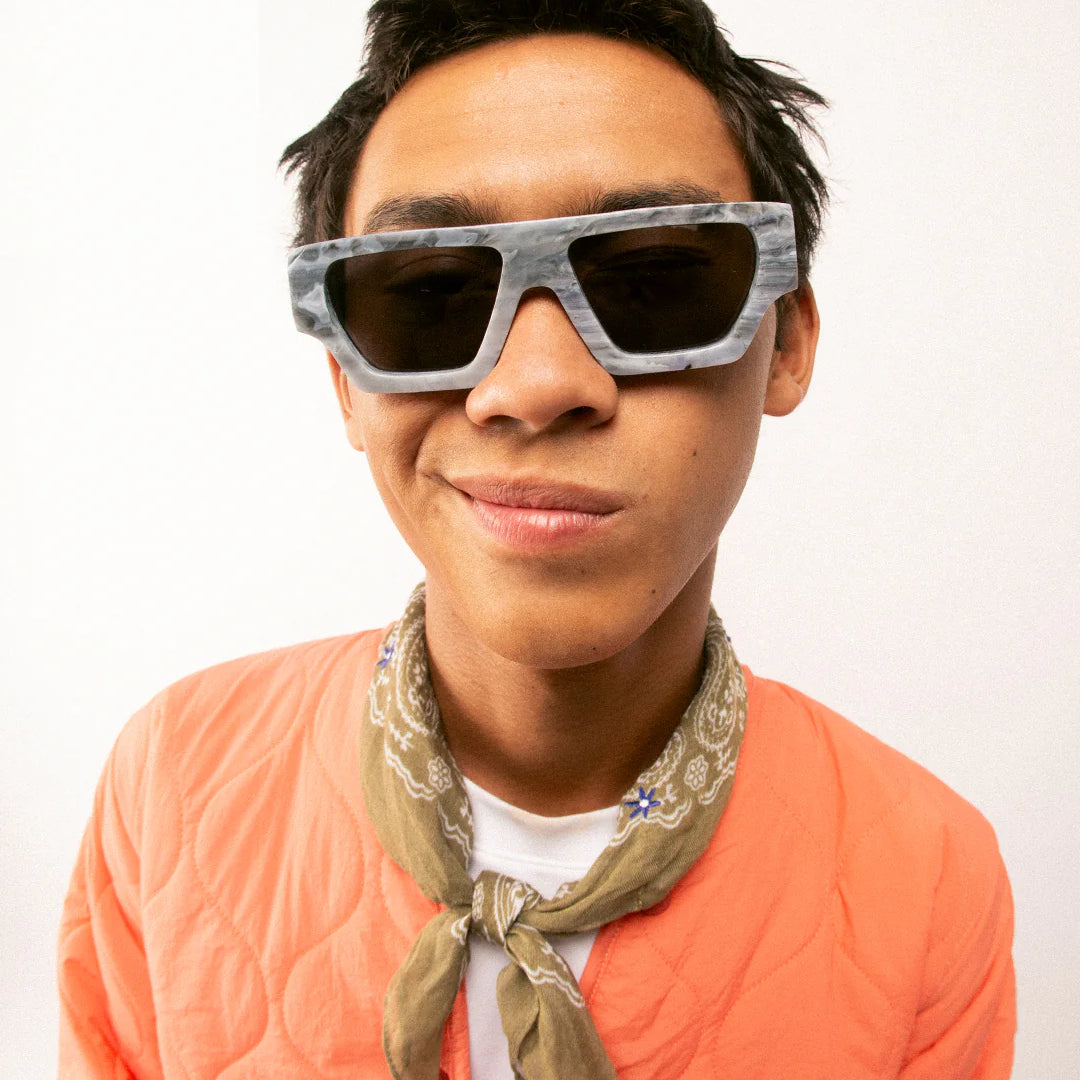 Person wearing sunglasses and an orange sweater with a bandana, on a white background