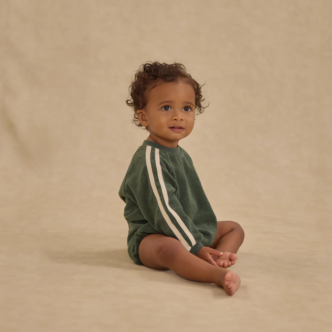 Child wearing a green onesie with white stripes on a beige background - Crewneck Romper Green by Rylee + Cru
