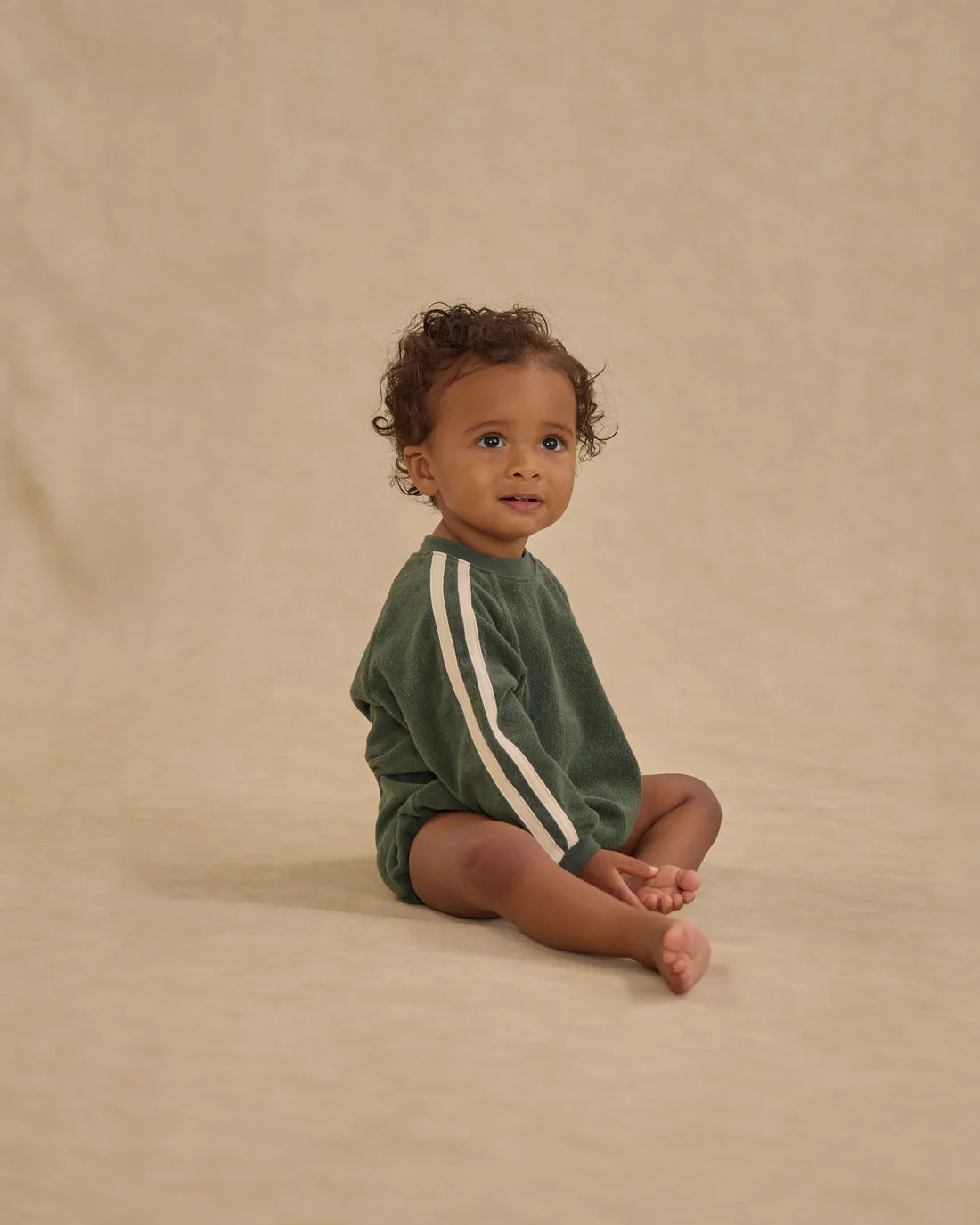 Child wearing a green onesie with white stripes on a beige background - Crewneck Romper Green by Rylee + Cru