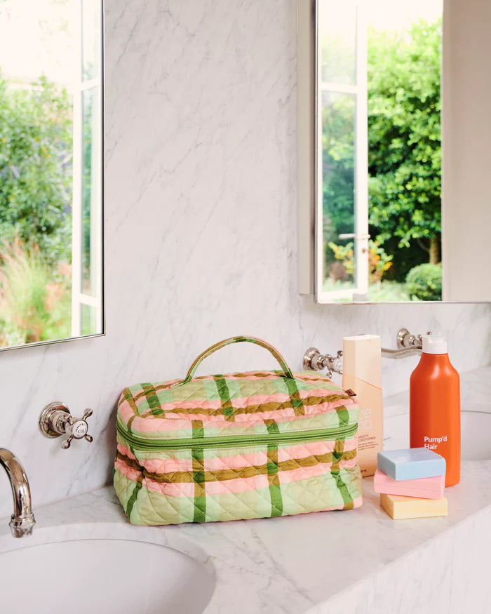 Plaid toiletry bag on a bathroom counter with various items from Kip & Co
