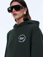 Close-up of moss green Aries Hoodie showing chest emblem and hood detail