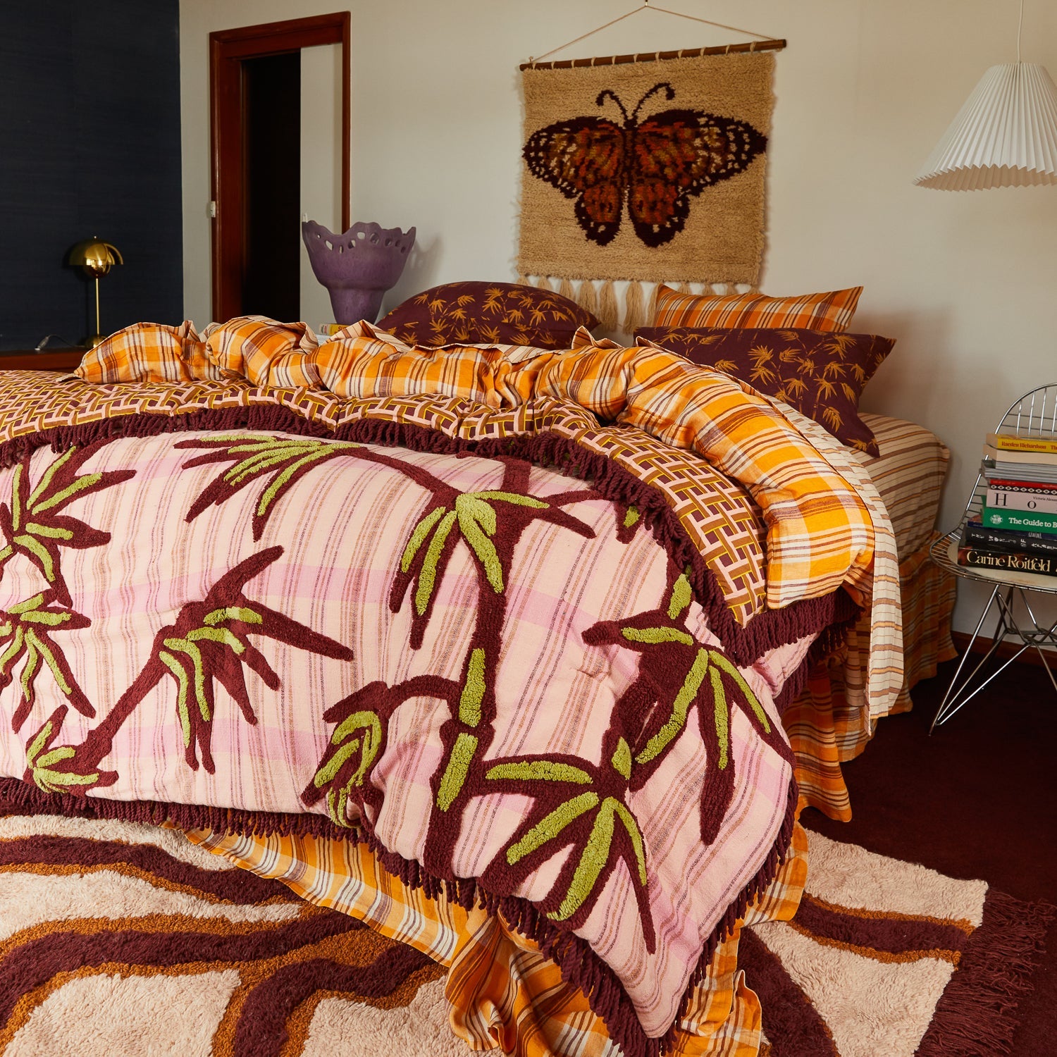 Sage Clare Aneta Tufted Blanket styled on bed with pink palm print and burgundy fringe in modern bedroom