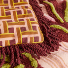 Aneta Tufted Blanket displayed on bed with geometric pattern panel and burgundy fringe border detail