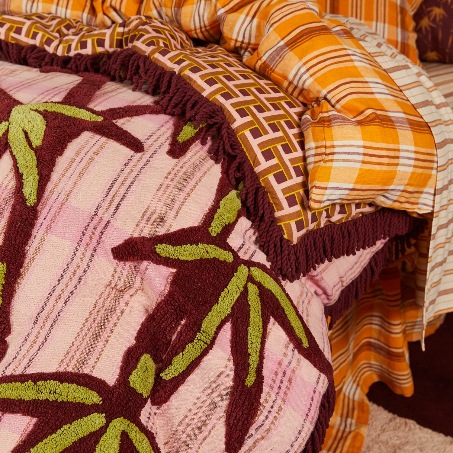 Close-up of chartreuse and burgundy tufted palm leaf details on pink striped Aneta blanket fabric