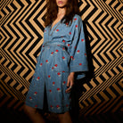 Three-quarter front view of light blue denim robe with red floral embroidery, tied belt, and front slit hem