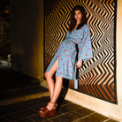 Full-length side view of light blue denim robe covered in red embroidered flowers, worn with platform sandals