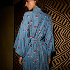 Back view of light blue denim robe showing red embroidered flower print, wide sleeves, and tie belt detail