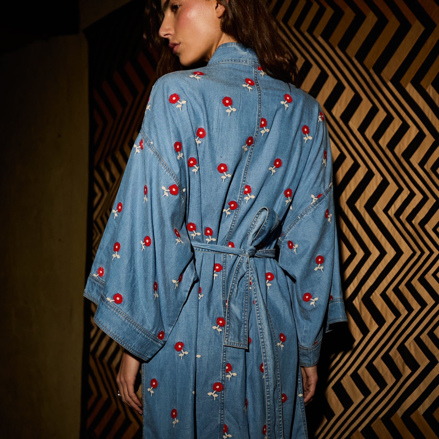 Back view of light blue denim robe showing red embroidered flower print, wide sleeves, and tie belt detail