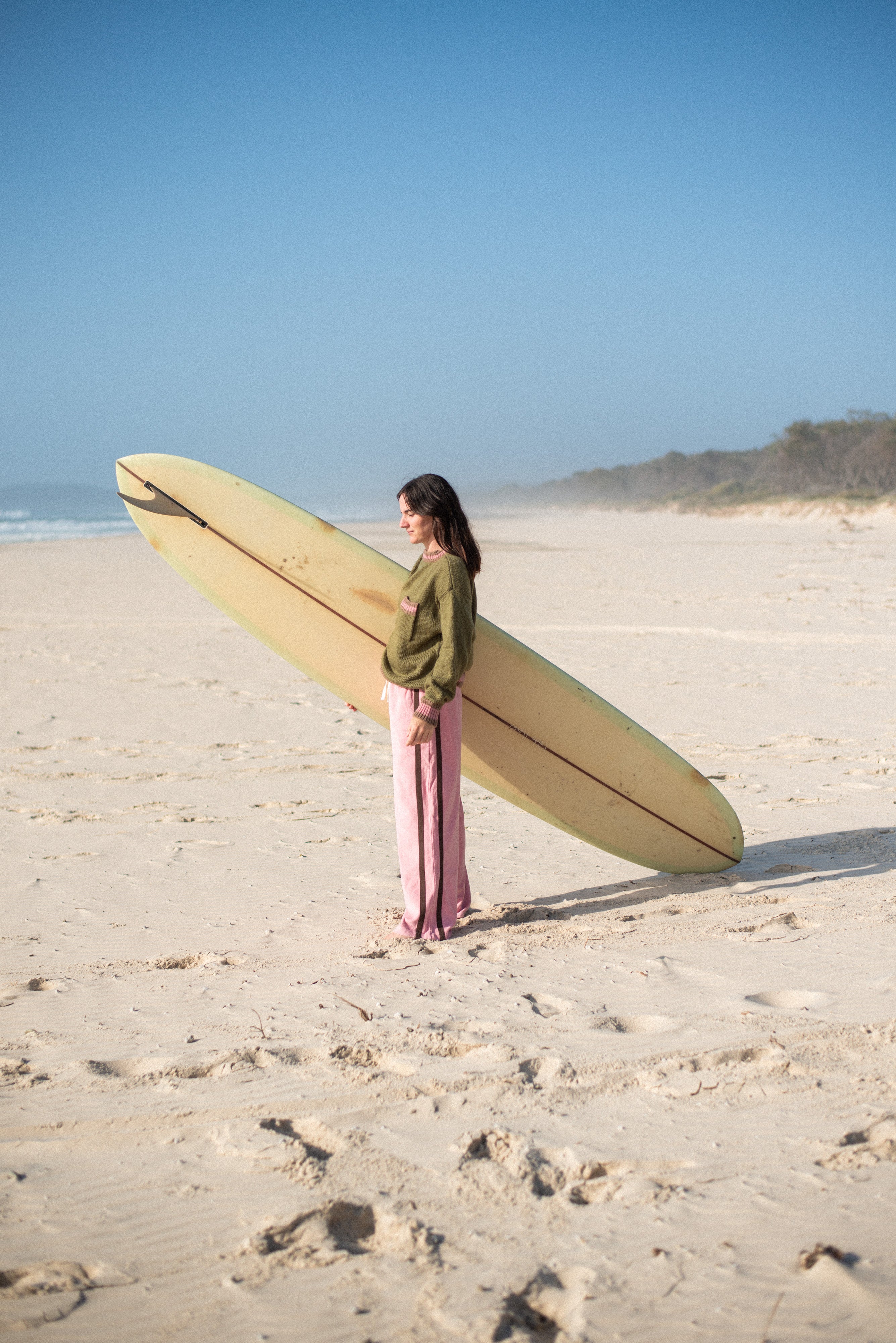 Model wearing blush pink Après Surf Panel Pants on beach holding surfboard in surf lifestyle setting