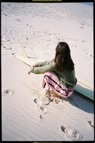 Back view of woman sitting on beach wearing Atmosea blush panel pants with dark side stripes