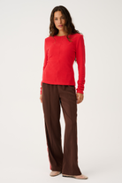 Full body front view of red Aspyn Top Siren styled with brown trousers showing complete outfit