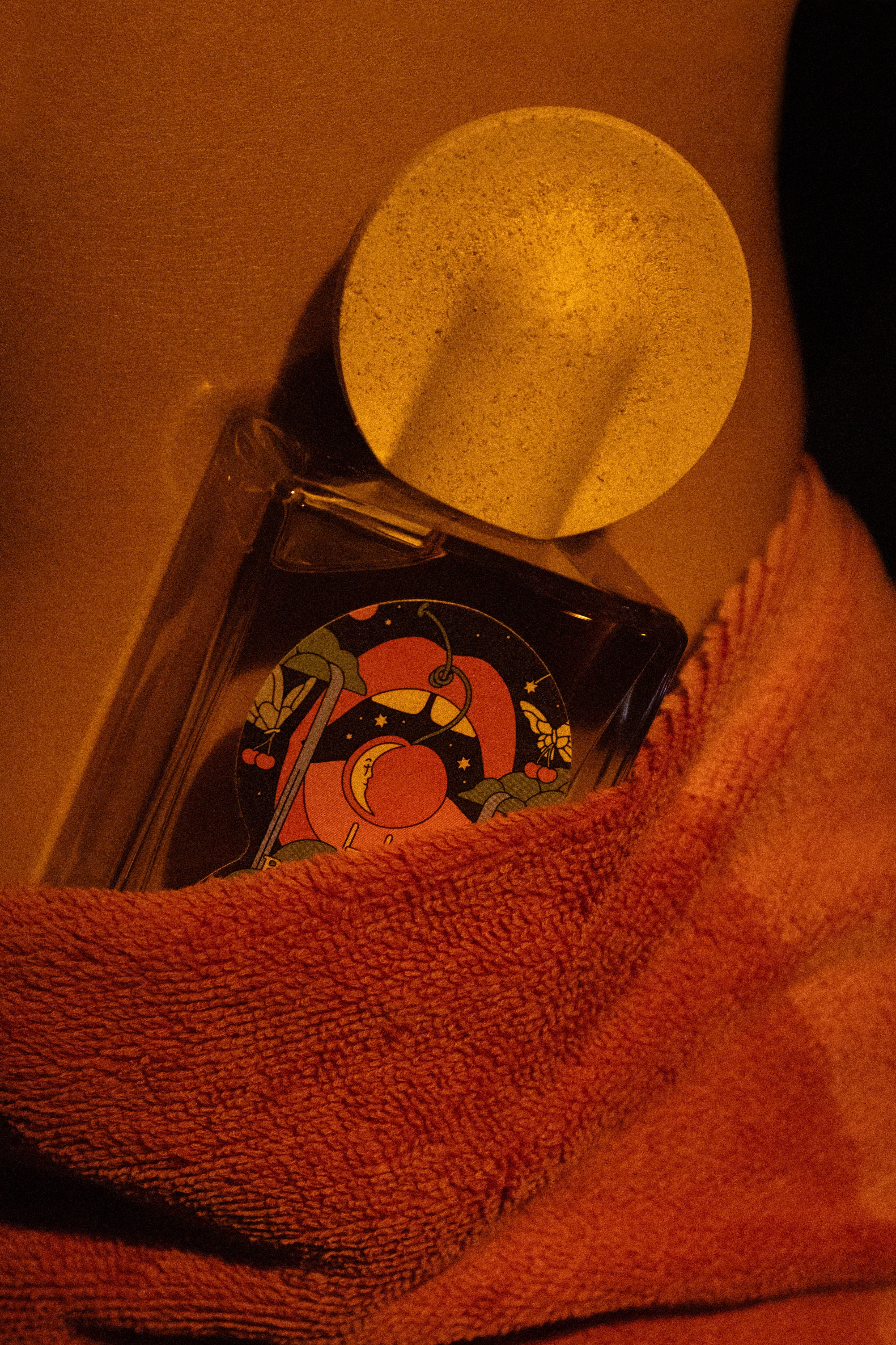Close-up of Bain De Minuit perfume nestled in coral textured towel with speckled cap visible