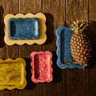 Colorful small trays in blue yellow coral pink with marbled resin finish styled with pineapple on wood surface