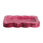 Crimson pink marbled resin small tray with scalloped wavy border, angled side view on white background