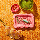 Crimson marbled resin small tray holding jewelry and lipstick, styled on a woven rattan surface with orchids