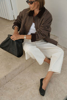 Woman sitting wearing moss green barn jacket with oversized fit and corduroy trim details
