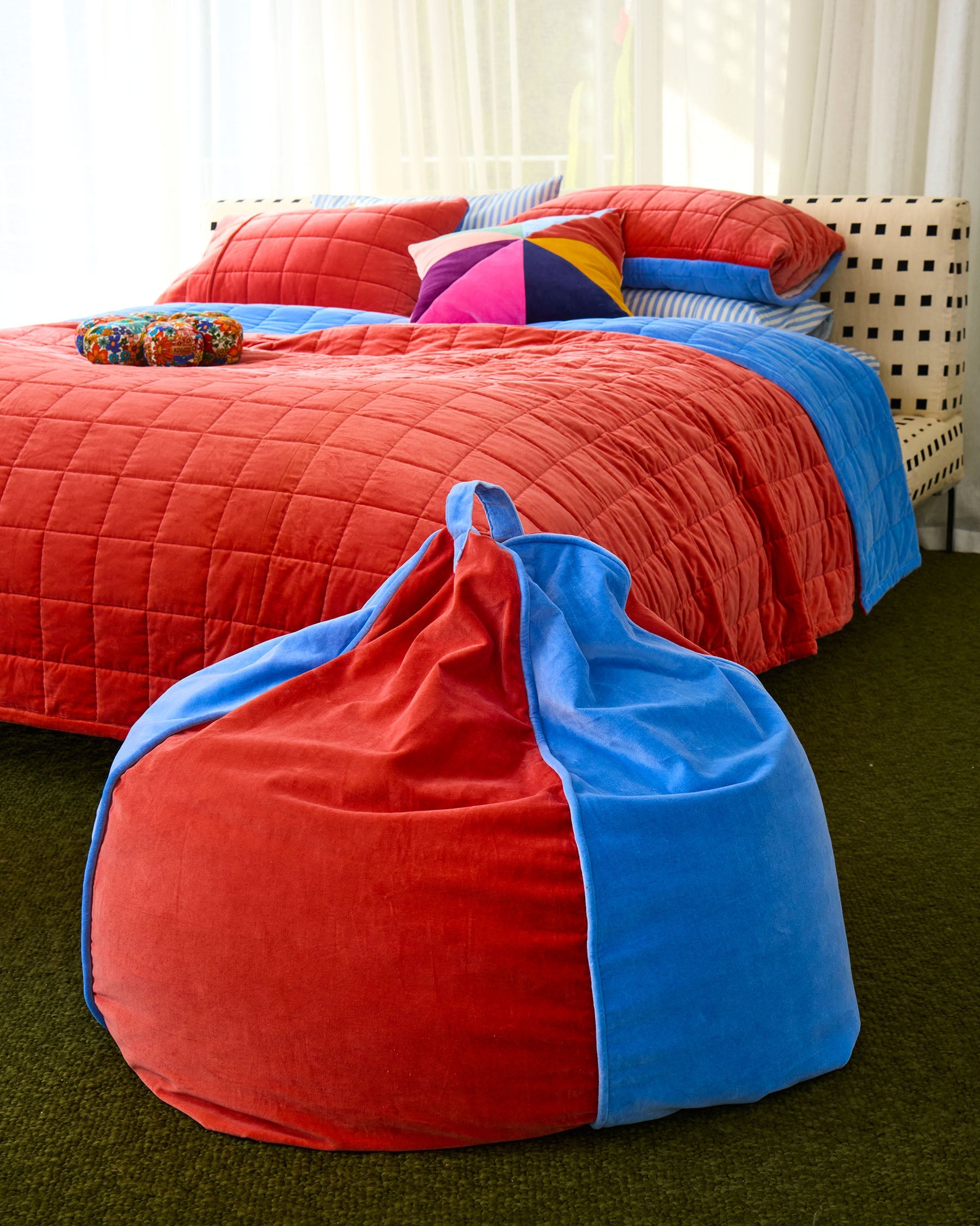 Blue Robin velvet beanbag placed beside bed with coral quilted bedding and colorful pillows