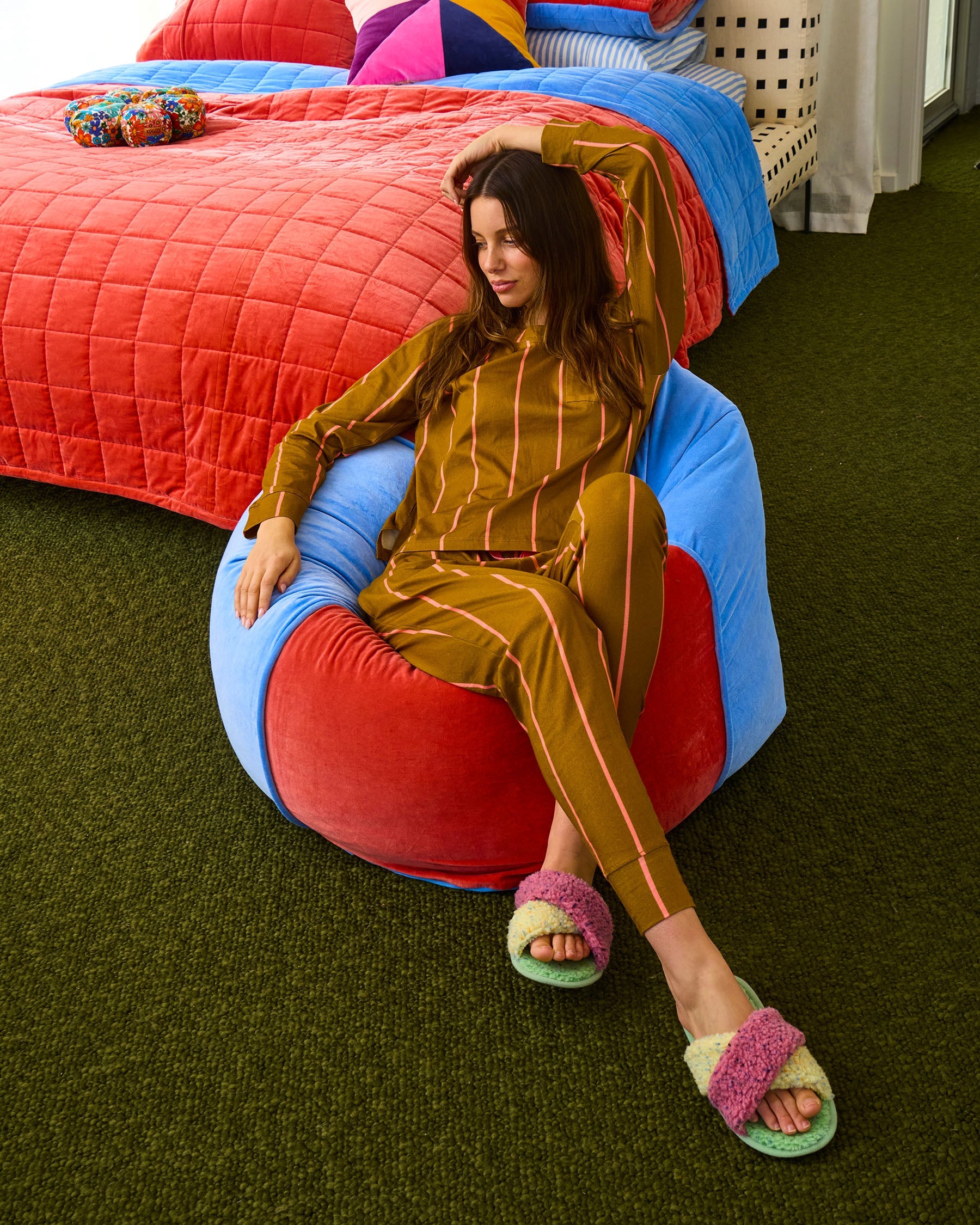 Adult woman seated on Blue Robin beanbag in modern bedroom with coral and blue bedding