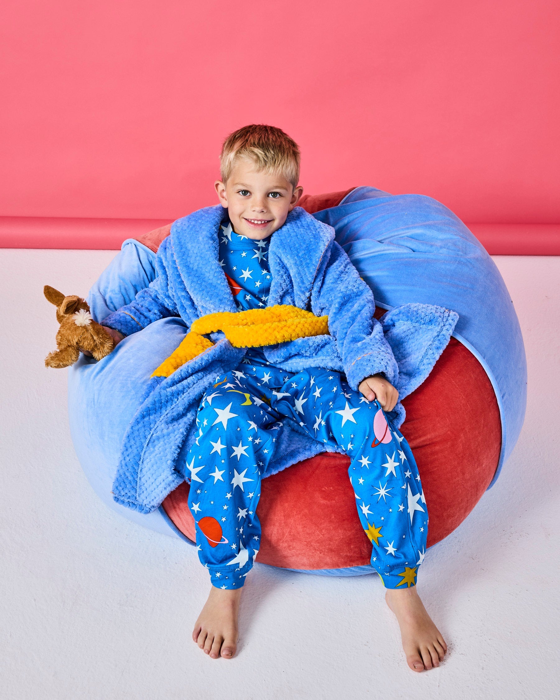 Young child sitting on Blue Robin beanbag wearing blue star pajamas with toy and blanket