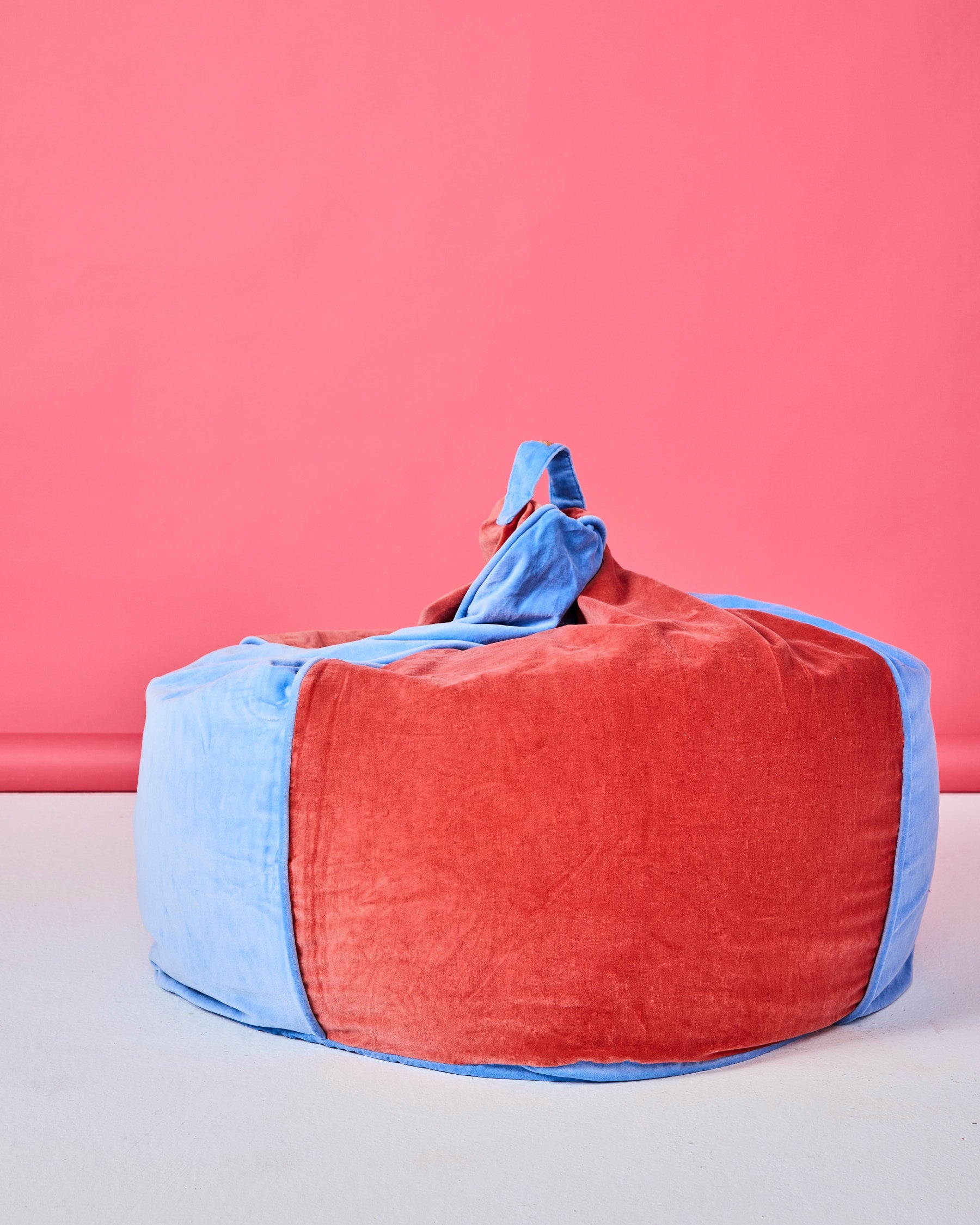 Blue Robin velvet beanbag with coral handle detail against pink studio background