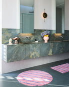 Modern bathroom featuring round Blushing Stripe Bath Mat by Kip Co on dark tile floor with marble vanity