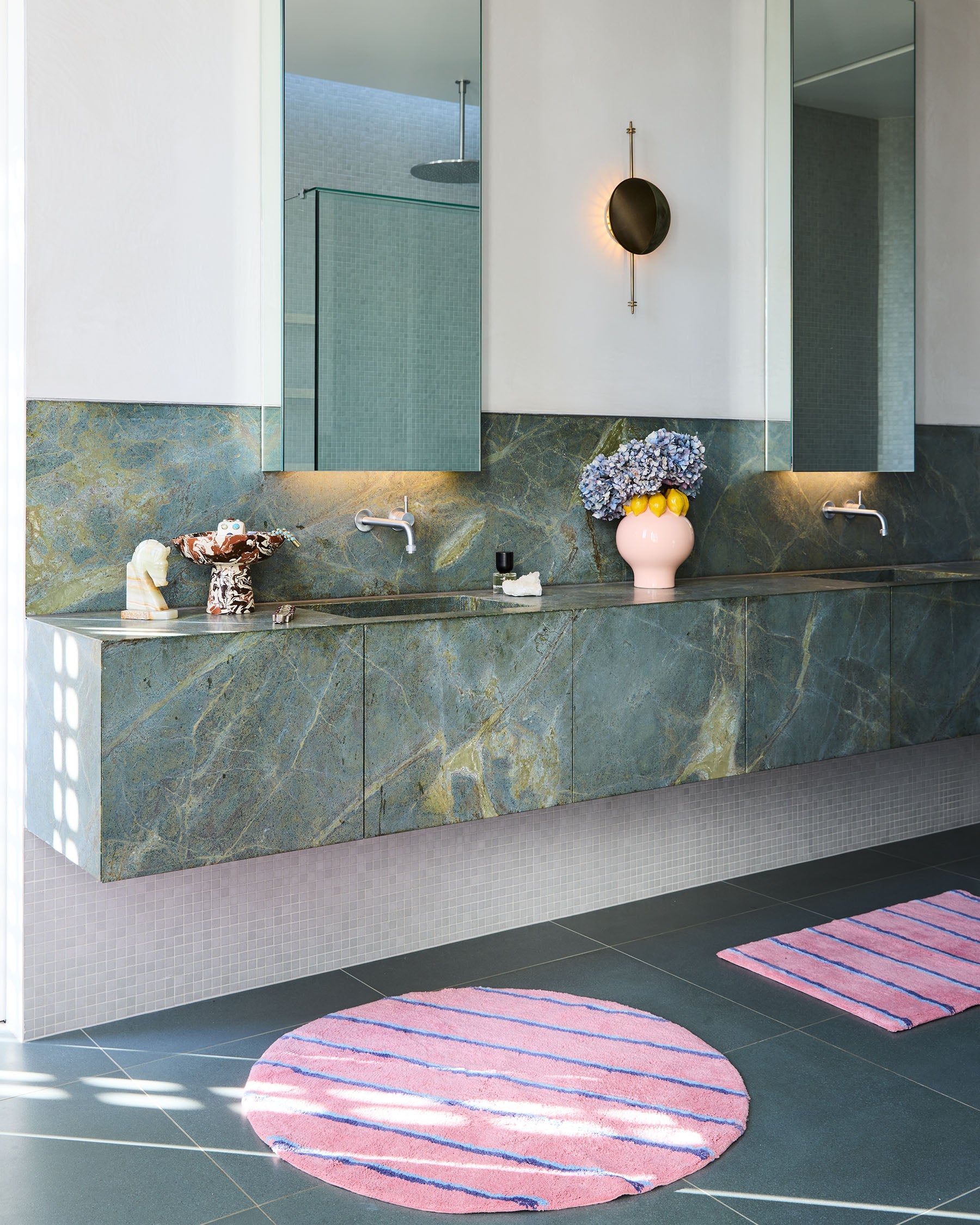 Modern bathroom featuring round Blushing Stripe Bath Mat by Kip Co on dark tile floor with marble vanity